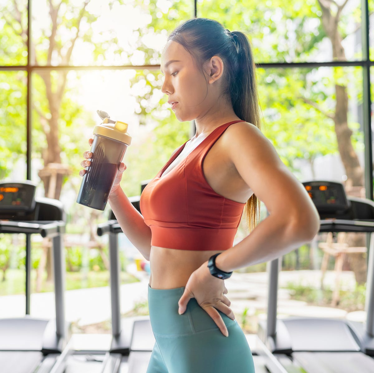 Woman in athletic wear holding a shaker bottle in a gym setting